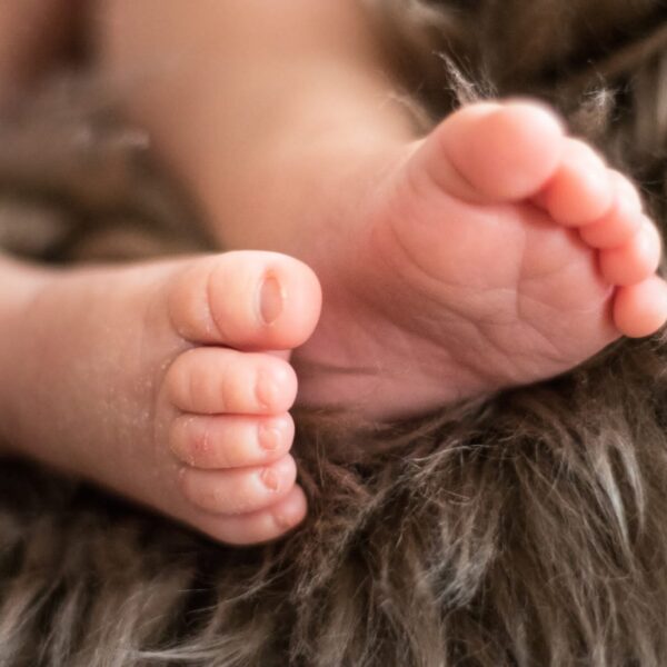 Zarte Szene zur Geburt und Taufe – ein neugeborenes Baby in weißen Tüchern, liebevoll gehalten, umgeben von natürlichen Elementen wie Wasser, Blumen und Licht