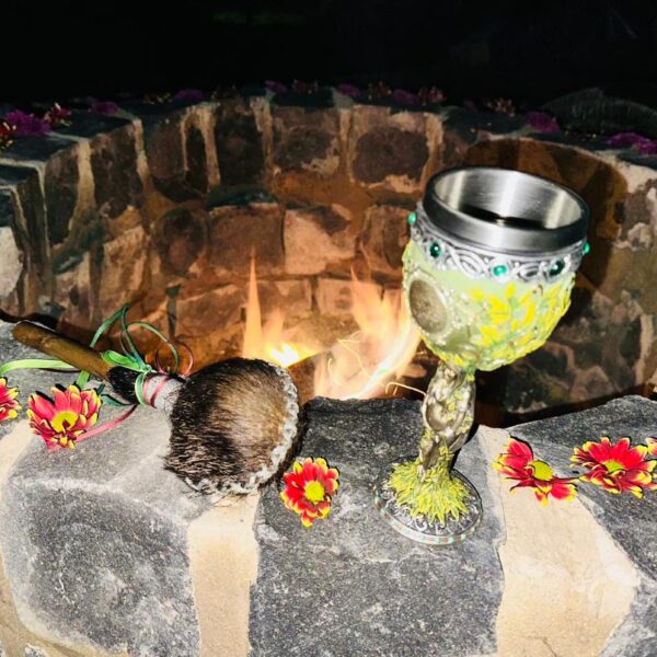Pachamama Schamanisches Ritual am Feuerplatz bei Nacht – heilige Feuerstelle mit Blumen geschmückt, Räucherfächer und verzierter Ritualkelch im Vordergrund